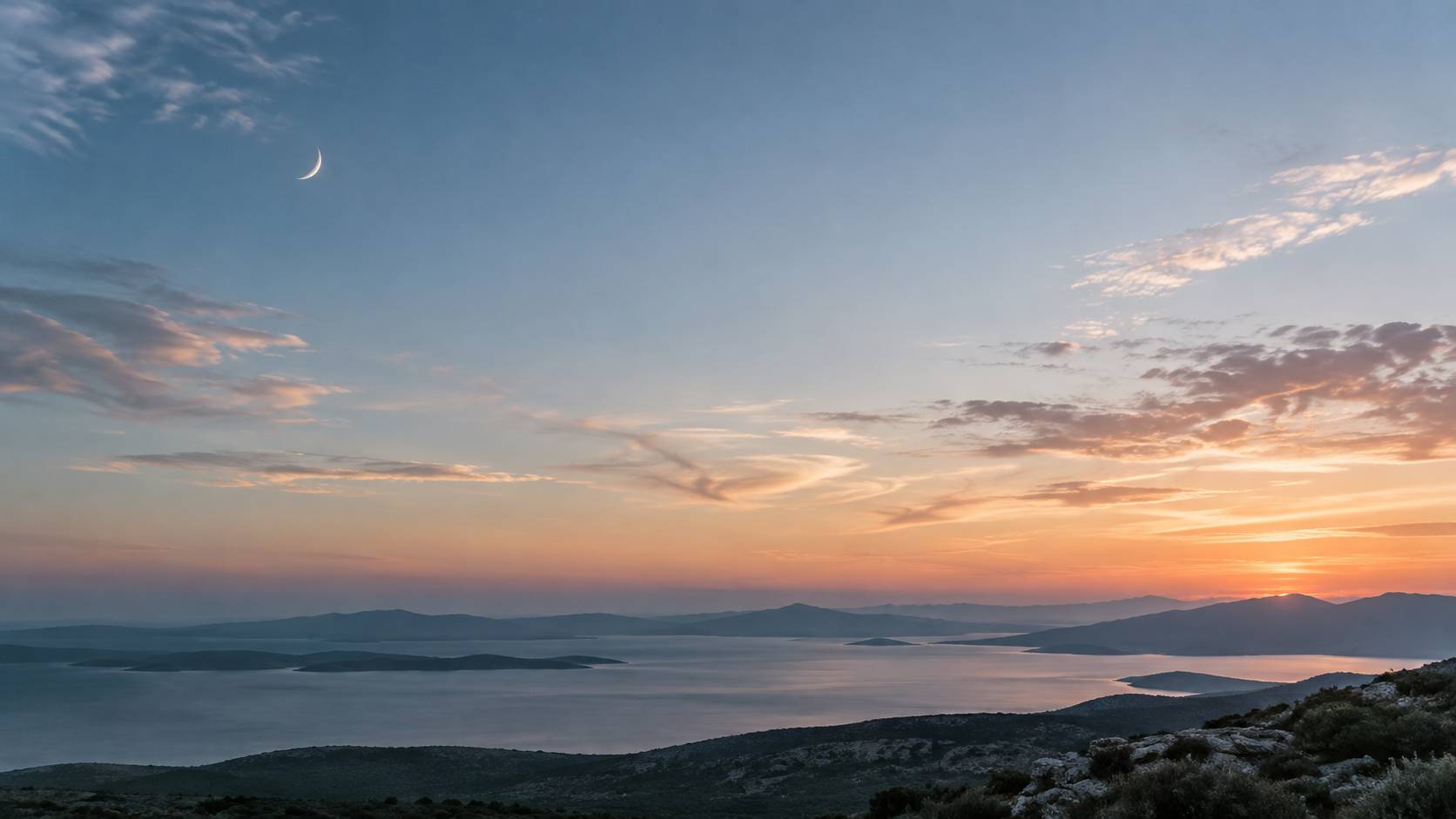 Ciel crepusculaire avec un fin croissant de lune au-dessus d'un paysage calme